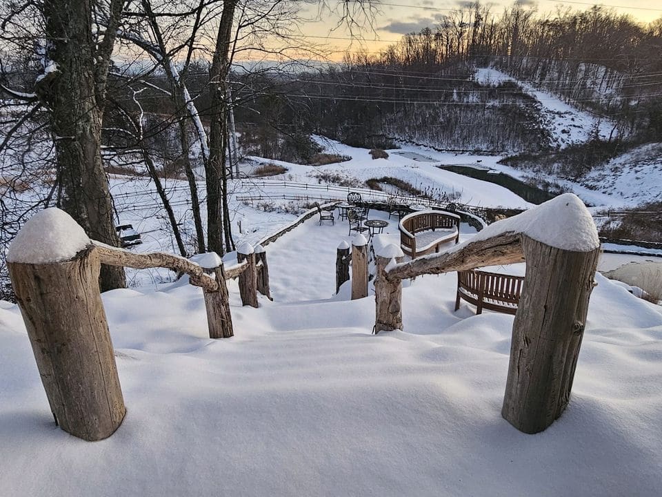 Snow-covered steps lead down to a magical landscape at Ancient Lore Village, where a distant river meanders under the glow of a sunset sky. A perfect scene to reflect on new beginnings and discover 5 ways to start your New Year with enchantment all around.