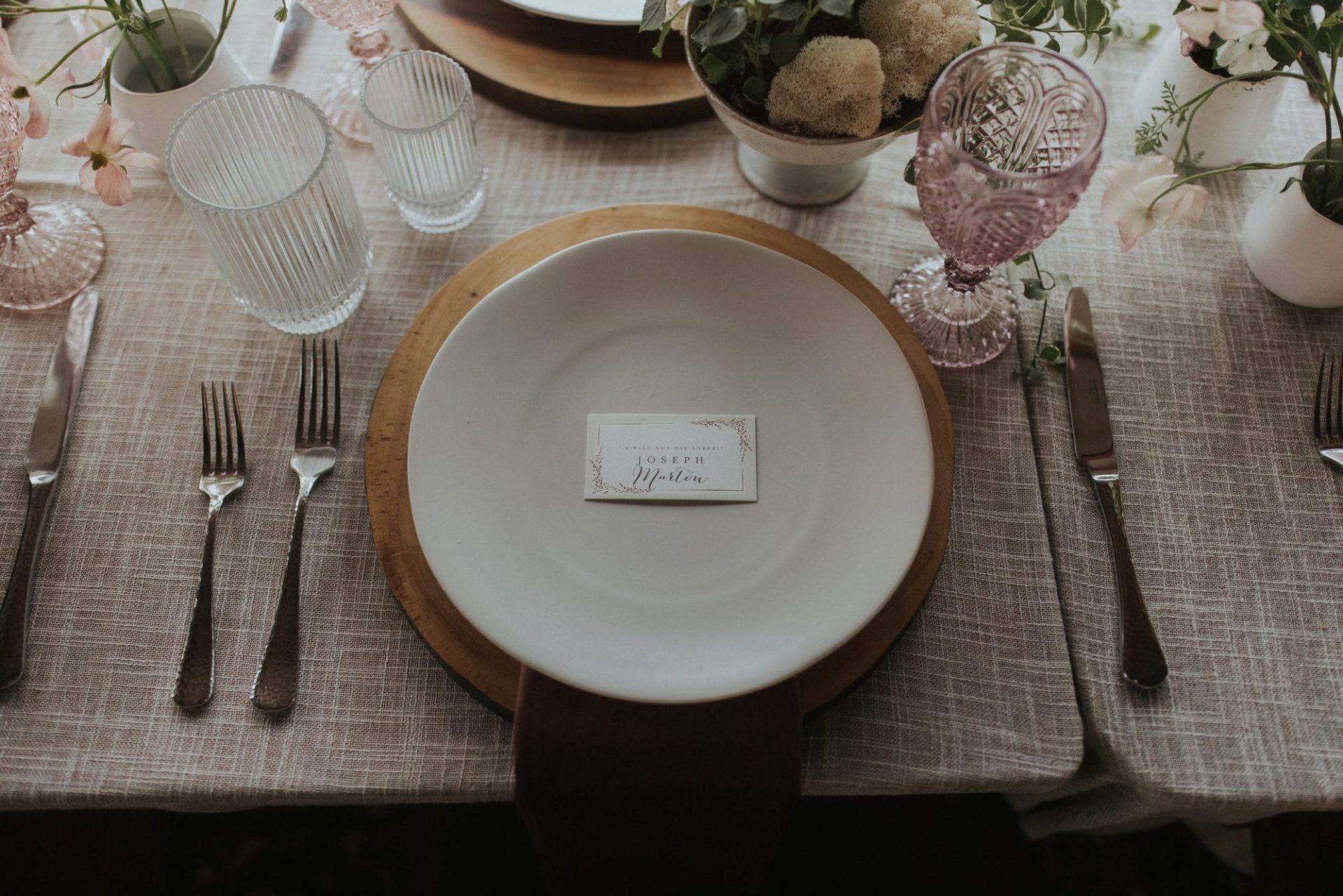 Elegant table setting with a white plate, utensils, glassware, and a floral centerpiece. A place card reads "Joseph.