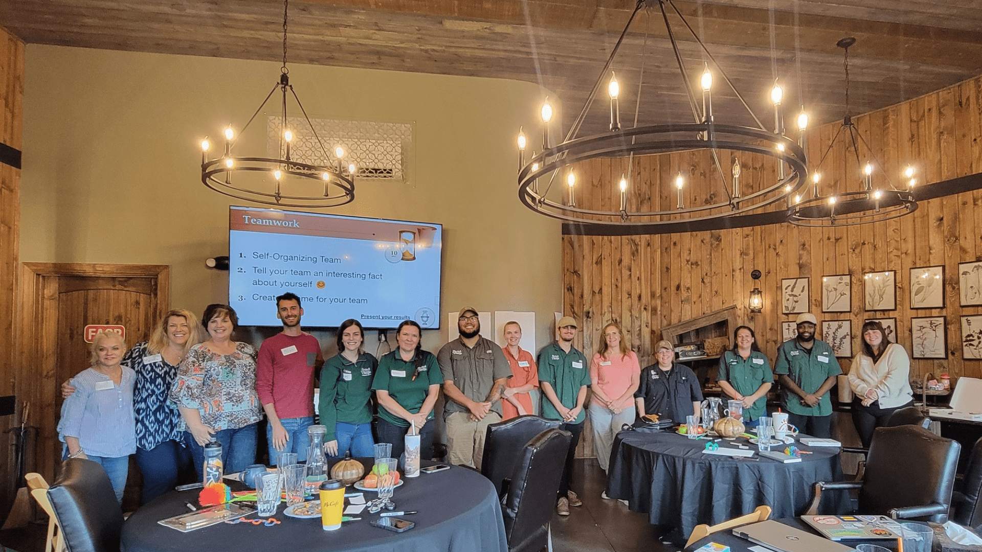 team A group of people in a conference room stands in front of a presentation screen with the word "Teamwork" displayed. Their focus is on team leadership and planning, driving empowerment through collective effort.